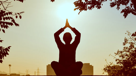 A woman practices meditation in front of a sunset after drinking Oomy mushroom tea.